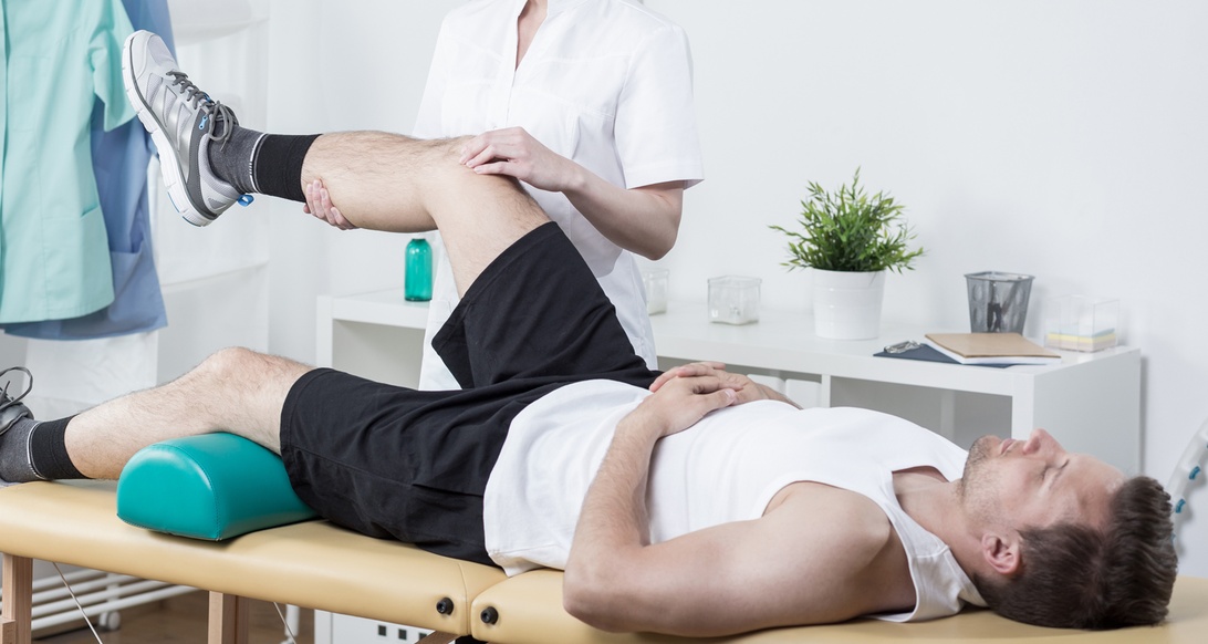 En fysioterapeut hjälper en patient med ben-terapi på en behandlingsbänk i en professionell rehabiliteringsklinik.